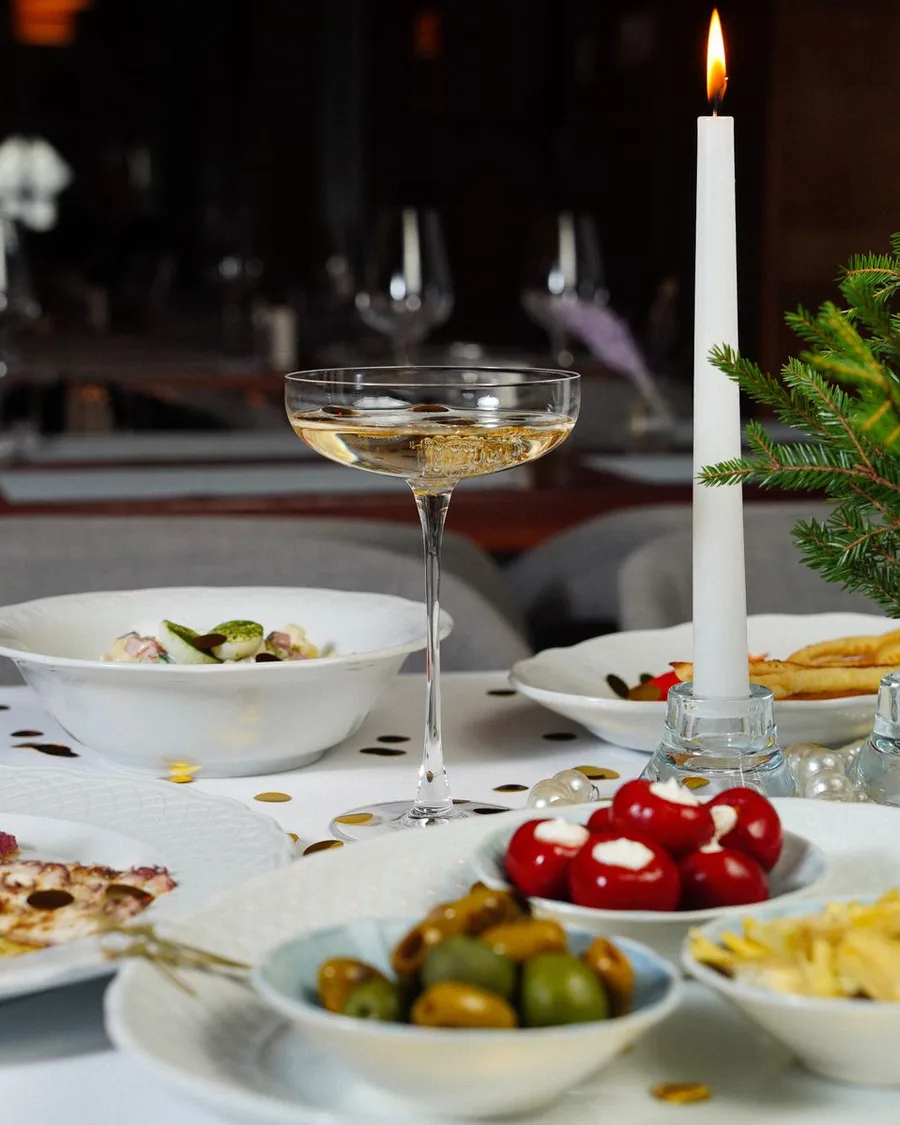 A candlelit holiday table with a coupe of sparkling wine, pine sprigs and appetizers