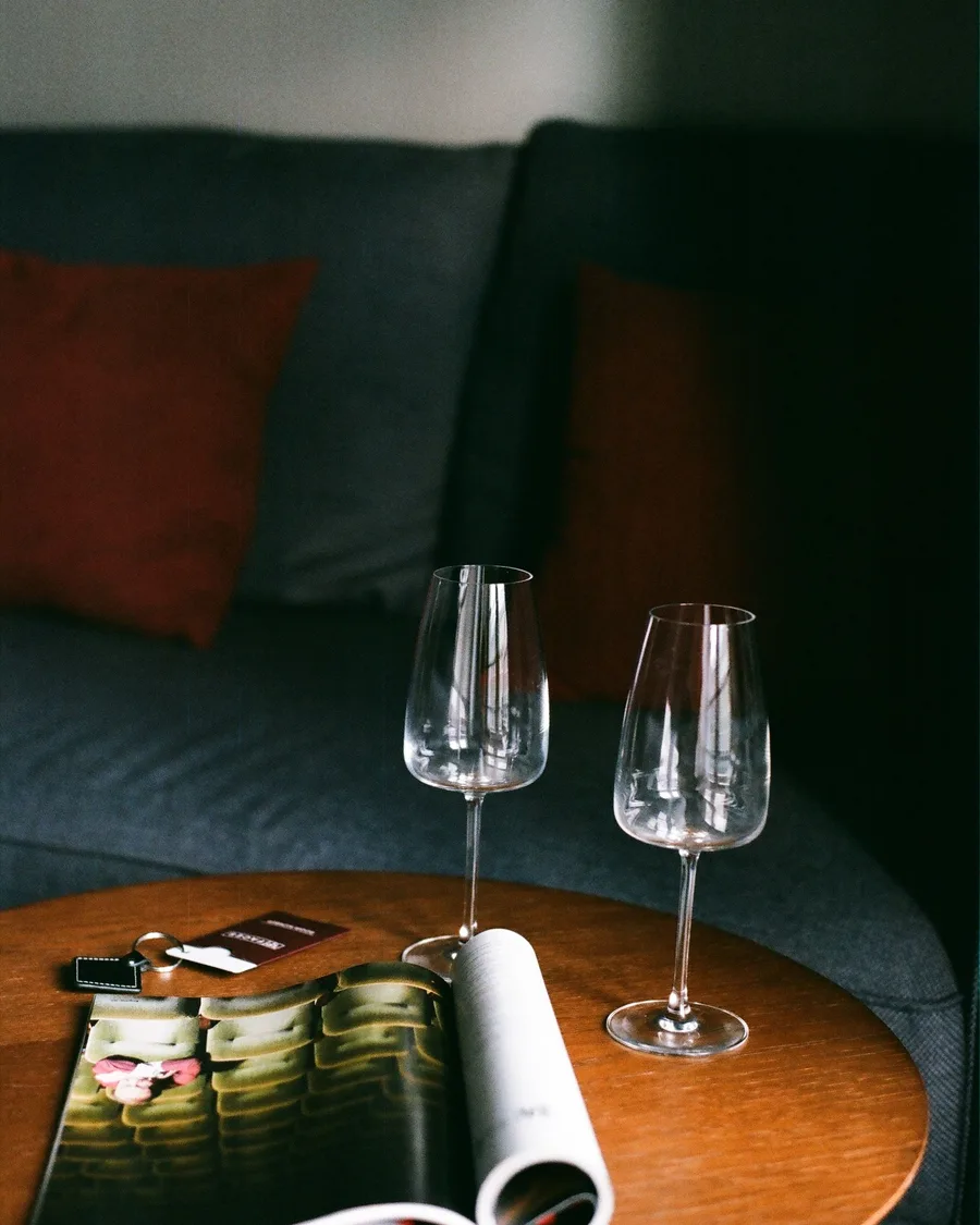 Two empty wine glasses and an open magazine on a wooden side table by a couch