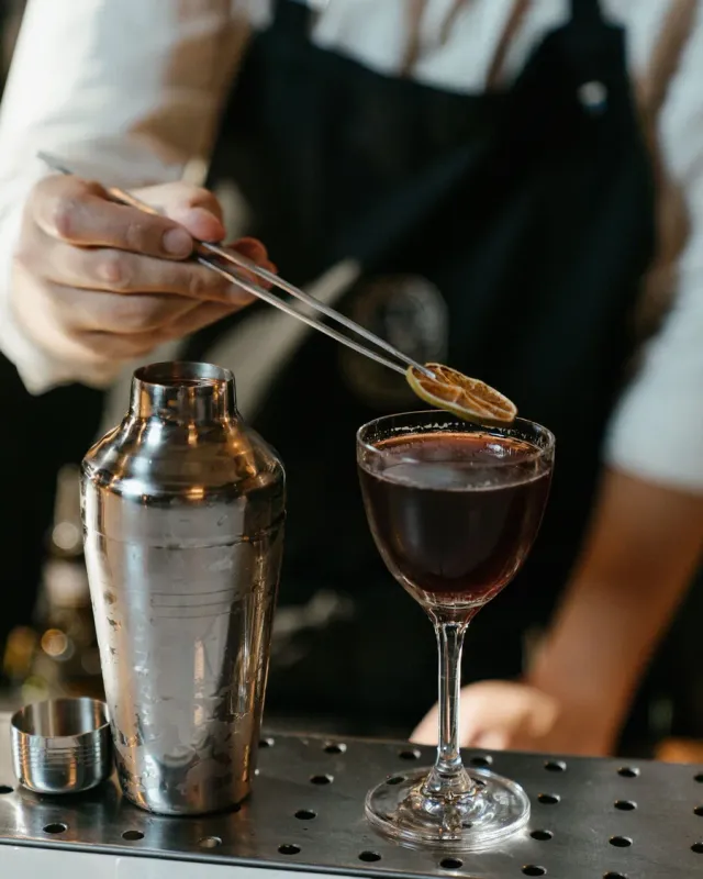 A bartender garnishing a dark coupe cocktail
