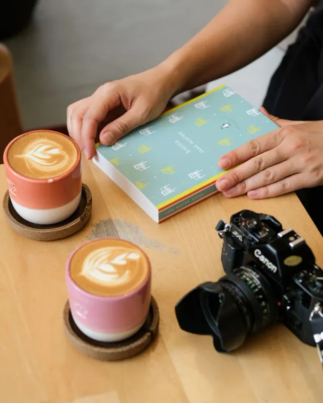 Two lattes, a book and a camera on a cafe table