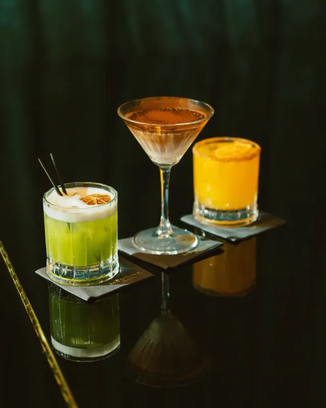 Three cocktails on a dark reflective bar