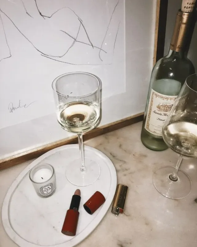 A glass of white wine on a marble tray beside a bottle