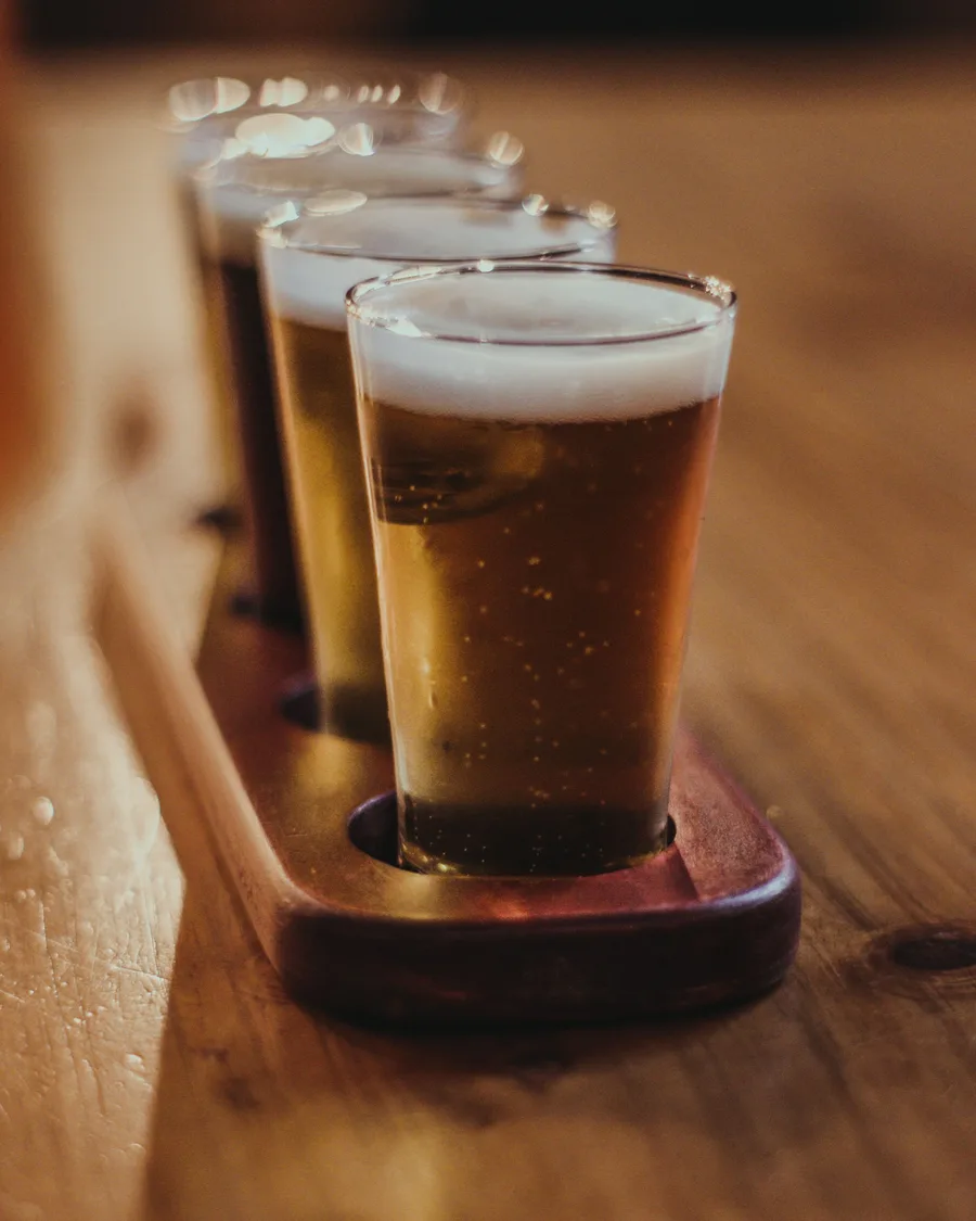 A flight of amber beers on a wooden paddle on a warm bar table