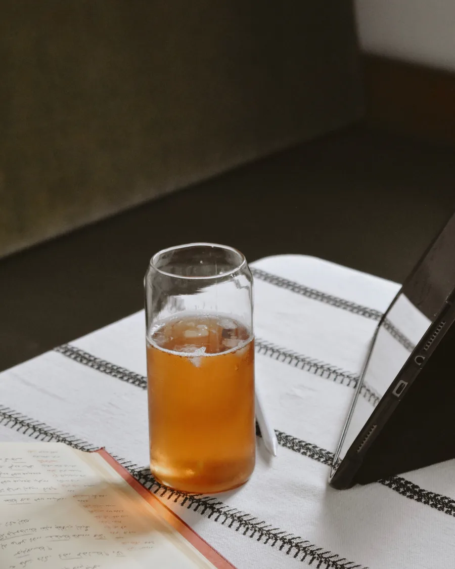 An iced amber drink beside an open handwritten journal and a phone on a striped tablecloth