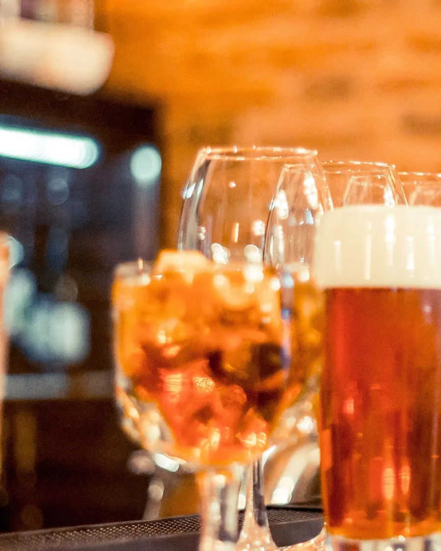 A spritz over ice, a glass of amber beer and wine glasses on a warm-lit bar